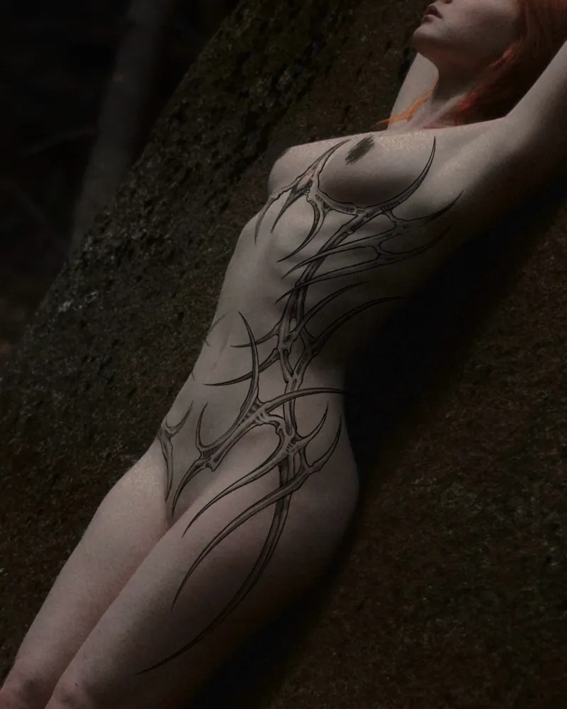 Tatuaggio nero cyber tribal sul braccio, con linee allungate e ramificazioni che seguono la spalla
