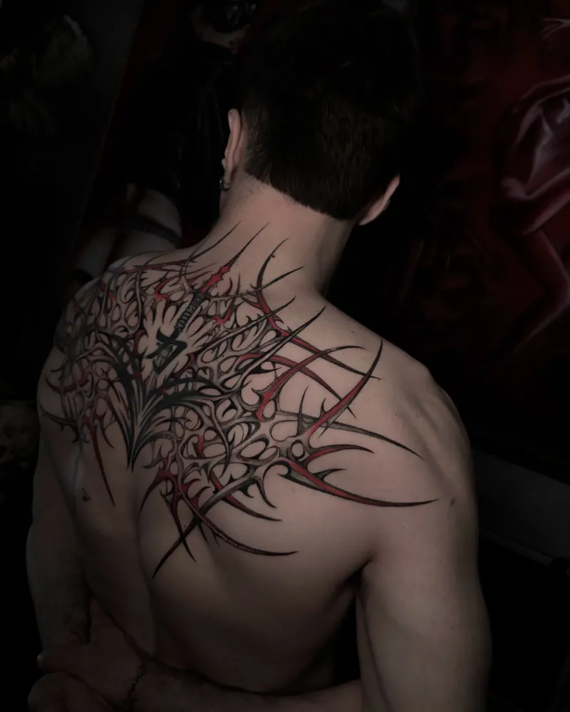 Tatuaggio cyber tribal sulla parte alta della schiena, con un nucleo centrale e linee che si aprono verso le spalle