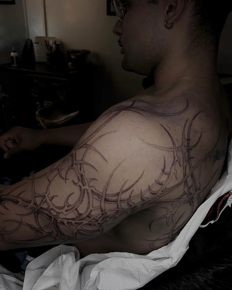 Composizione cyber tribal nera sul torace e sulla spalla, con punte curve e ampie porzioni di pelle non tatuata